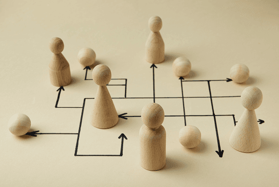 Wooden peg figures standing on a grid with directional arrows